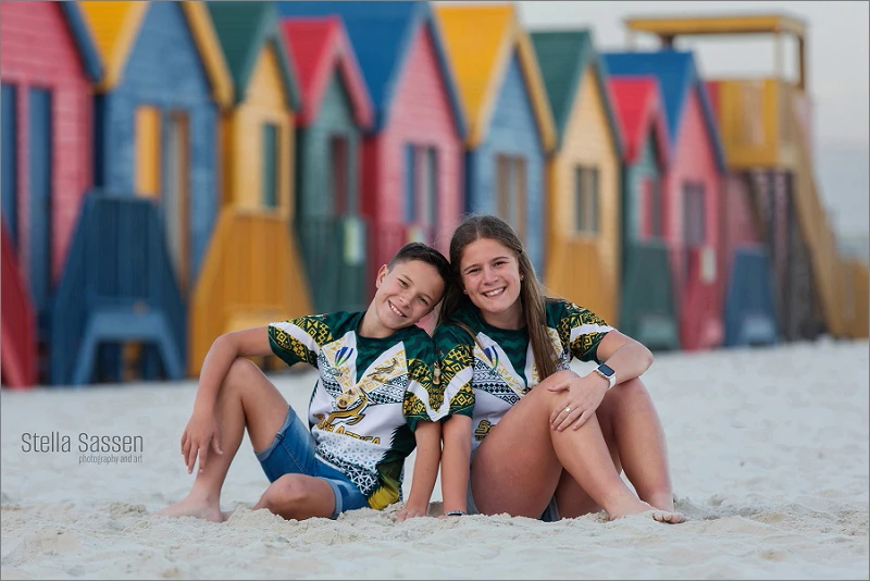 Teenagers posing in front of colourful wooden houses on Muizenberg beach in Cape Town